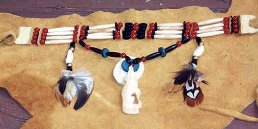 Choker, necklace presented on deerskin. 
Four leather strands carry beads symmetrically arranged from the center outward: 
Central red bead, black oval bead, leather separator, red bead, black washer, 
long white bi-conic buffalo horn bead, black washer, red bead, leather separator, 
red bead, long white bi-conic buffalo horn bead, red bead, leather separator, red 
bead, and white beaded section for closing. 
Hanger string extending downwards from leather separators between the two red 
beads between the white buffalo horn beads, symmetrically from the center out- and 
upward: turquoise blue bead, black oval bead, red round bead, long black oval bead, 
turquoise disk, long black oval bead, red bead, oval black bead. Hanger at the 
middle at blue bead showing frontal: blue disk - twice the size of the blue disk in 
hanger string - on upper half of twice as big white bone or horn disk. Sitting Wolf 
of carved white bone howls into the blue disc center as to the moon. 
Hanger left and right of the hanger string - extending from between the red bead 
and the white bone: black oval bead, metallic bead, thick white horn oval bead, 
metallic bead, black oval bead, various beautifully colored small feathers.
