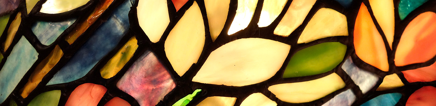 Stained glass, fragment. Leadlight image, showing organic leaf-forms in bright colours of greenish yellow and green, framed in irregular leave-shaped black boundaries. Source 2022 August: Funderal & Cremation, Woodlawn Mission Funeral Home, www.dignitymemorial.com